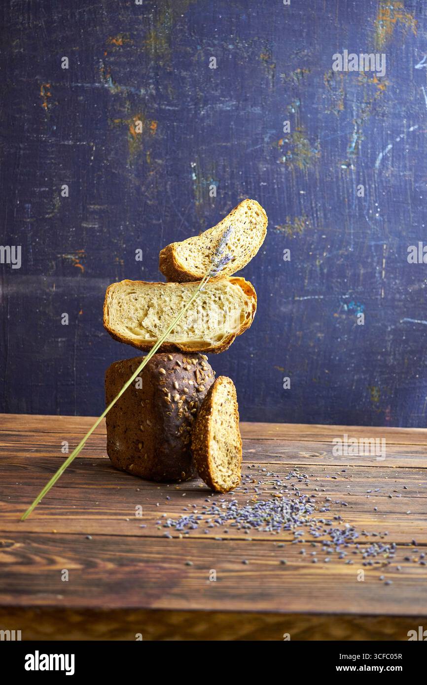 Kreative konzeptionelle Komposition mit ausbalancierten handwerklichen Brotscheiben auf rustikalem Holztisch, vor strukturiertem dunklem Hintergrund. Moderne Lebensmittelfotografie Stockfoto