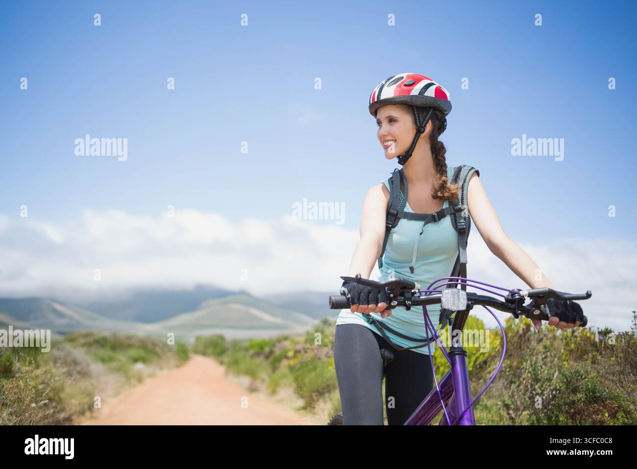 Hispanische Frau, die Fahrrad auf dem Feldweg fährt, mit Helm, fingerlosen Handschuhen und Rucksack, Kopierraum Stockfoto