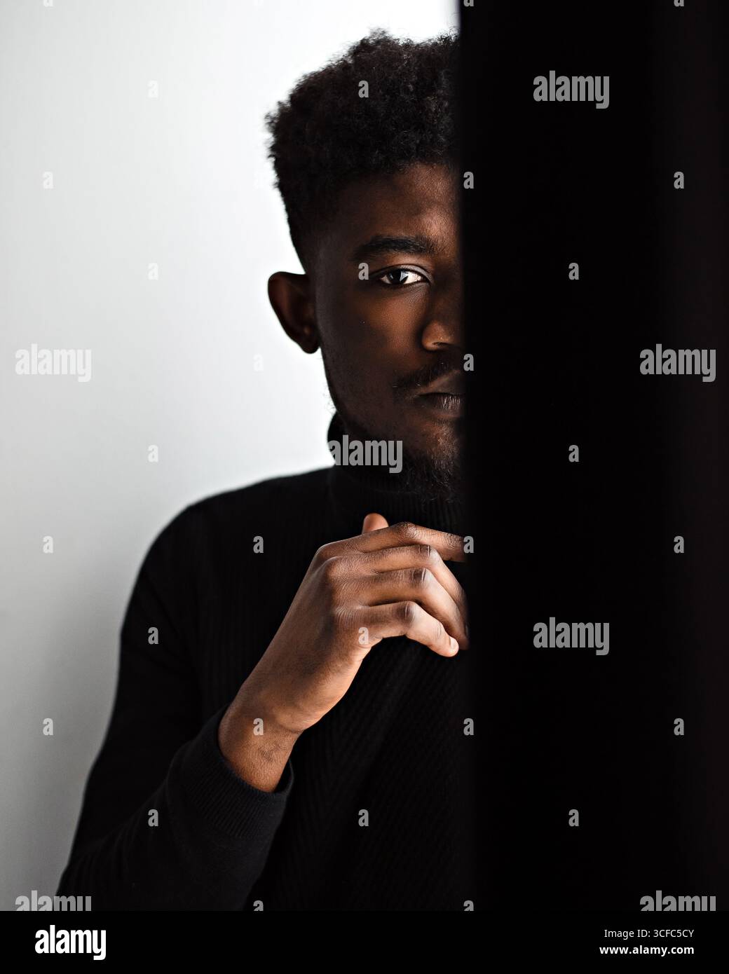 Teilweises Bild eines traurigen schwarzen Mannes. Lockiger junger bärtiger Kerl in Depression und Blick auf die Kamera. Person trägt schwarzen Pullover Stockfoto