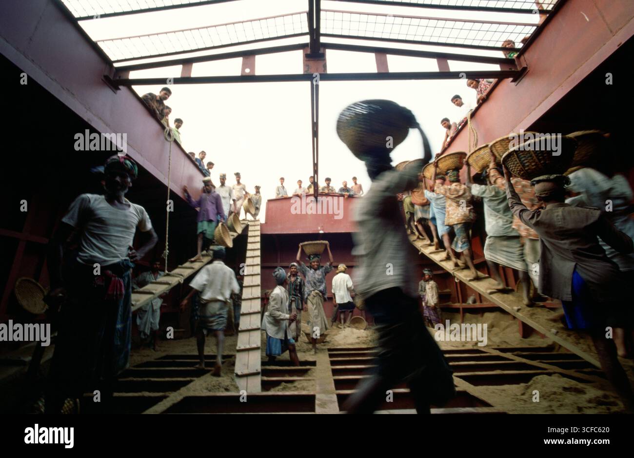 Die Arbeiter entladen ein mit Sand gefülltes Schiff, indem sie den Sand in Korbkörben auf ihren Köpfen tragen Stockfoto