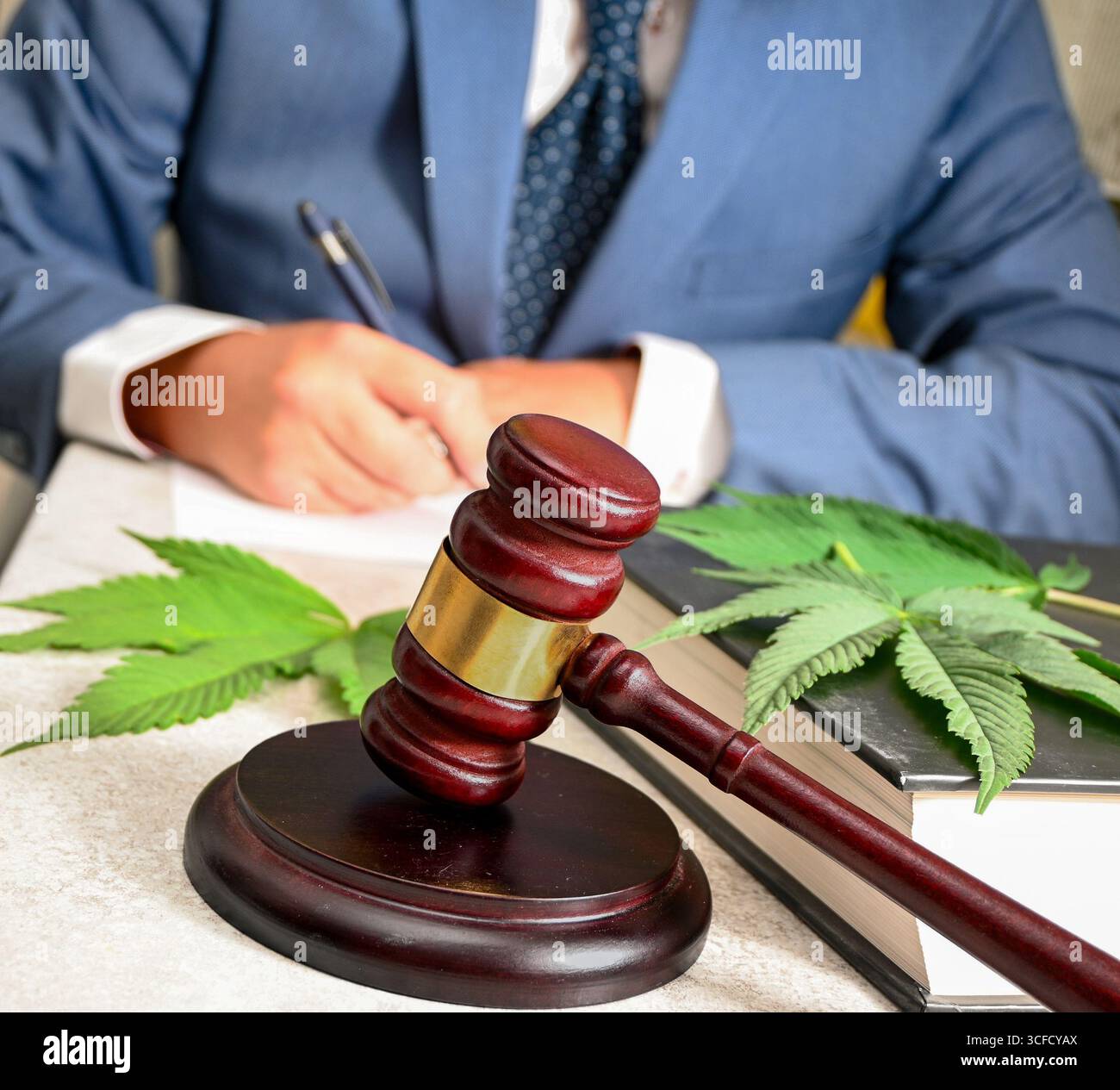 Der Anwalt unterschreibt ein Dokument für die Cannabislegalisierung mit Holzgabel und Marihuanablatt auf dem juristischen Buch. Stockfoto