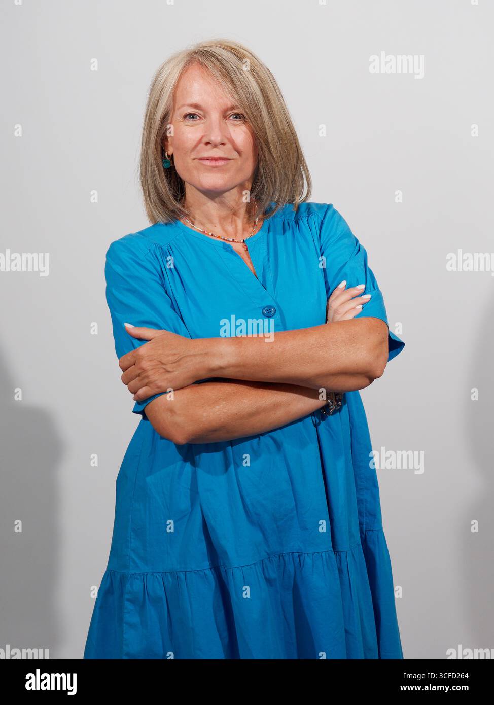 Eine selbstbewusste reife Frau in einem hellblauen Kleid mit überkreuzten Armen vor einem schlichten Hintergrund. Italien Stockfoto