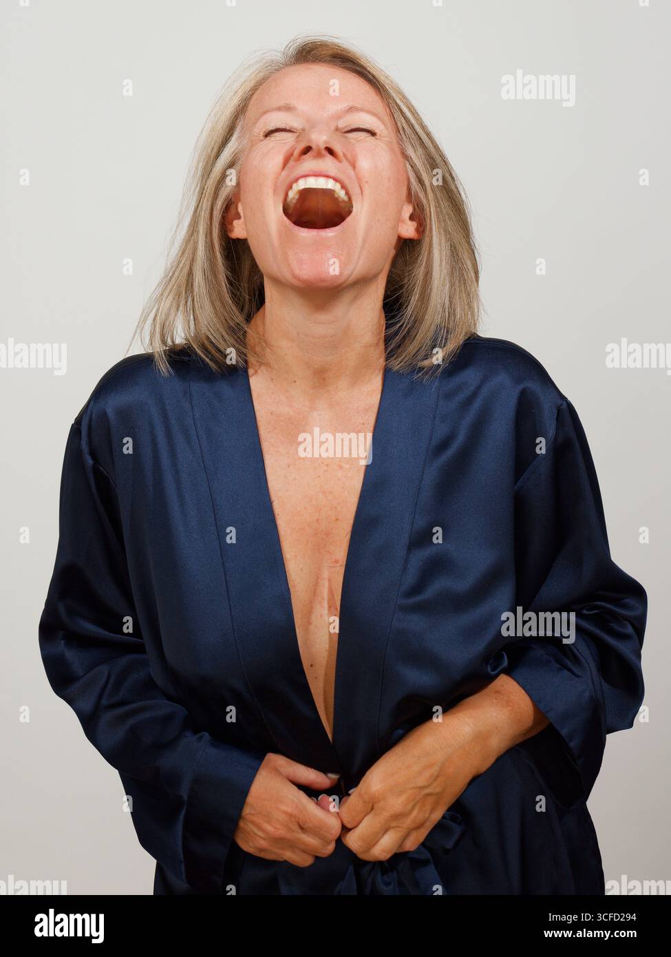 Reife Frau lacht in einem dunkelblauen Seidenmantel vor neutralem Hintergrund. Italien Stockfoto