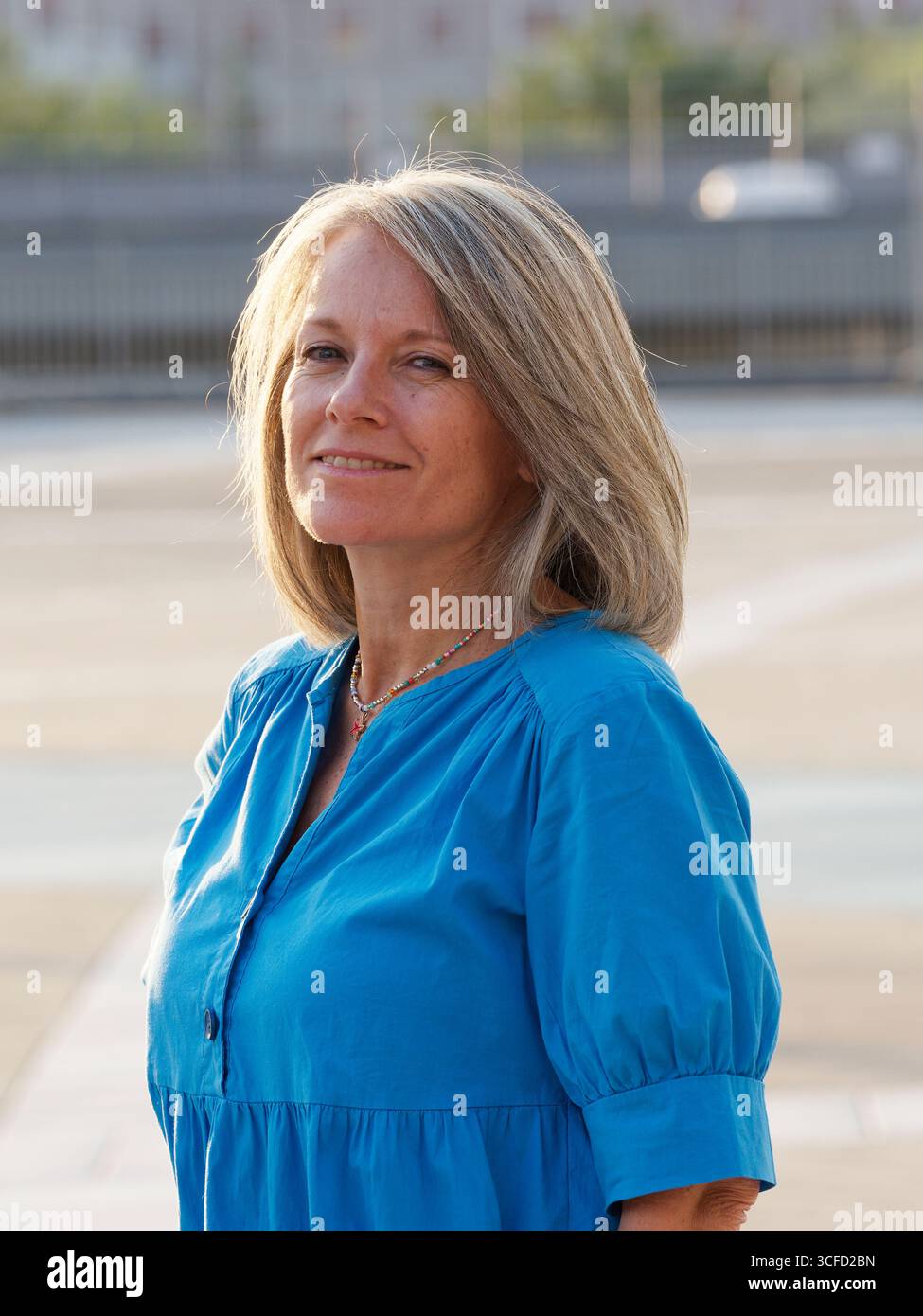 Frau in blauem Kleid posiert draußen mit Hand auf Hüfte und lächelt selbstbewusst in die Kamera. Italien Stockfoto