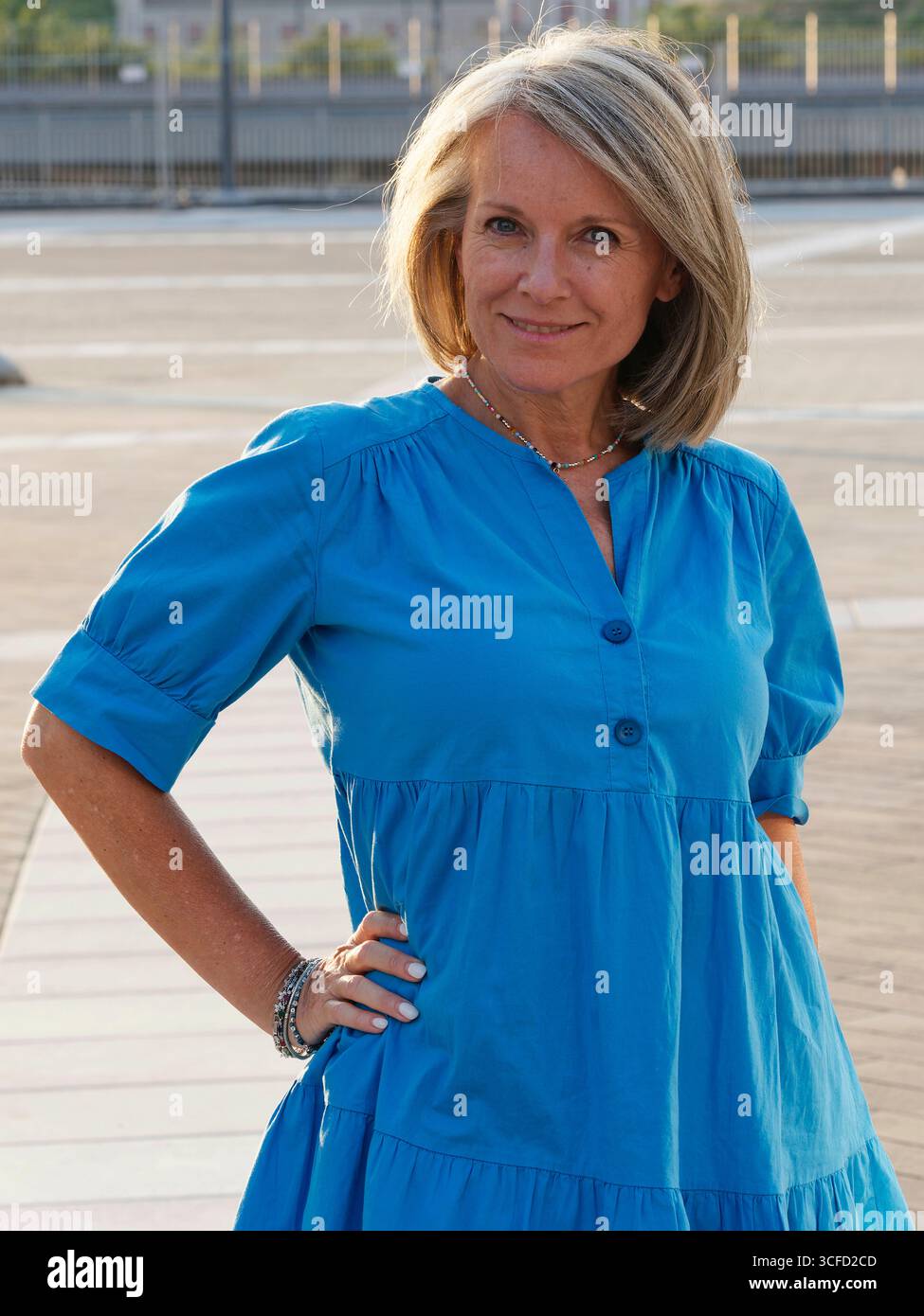 Frau in blauem Kleid posiert draußen mit Hand auf Hüfte und lächelt selbstbewusst in die Kamera. Italien Stockfoto