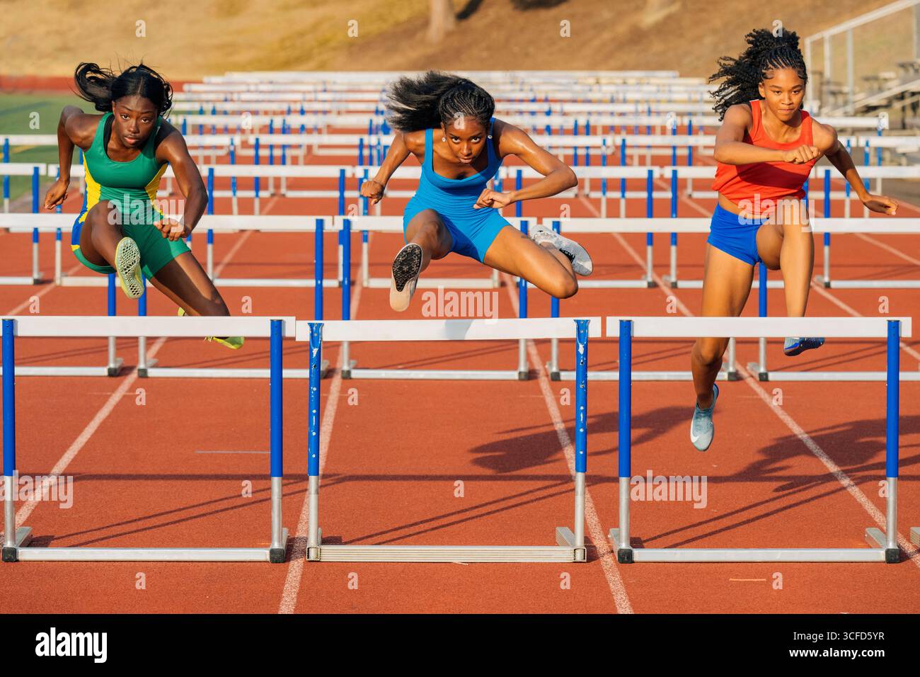 Drei junge Athletinnen in bunten Outfits springen auf einer Strecke Hürden. USA Stockfoto