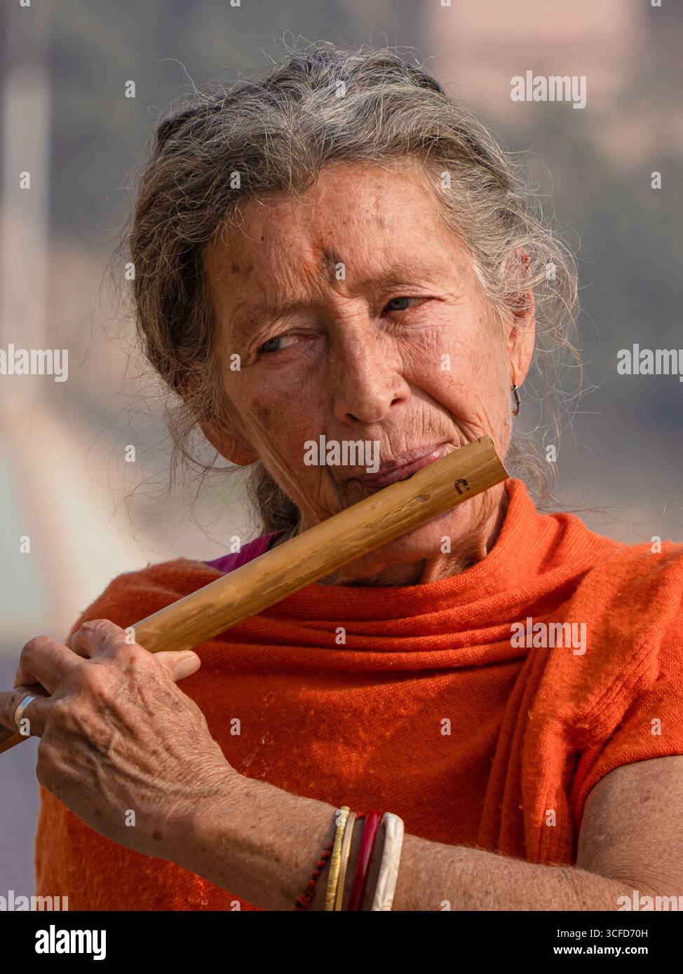 Porträt einer älteren westlichen Frau, die eine Holzflöte auf den Ghats in Varanasi spielt. Stockfoto