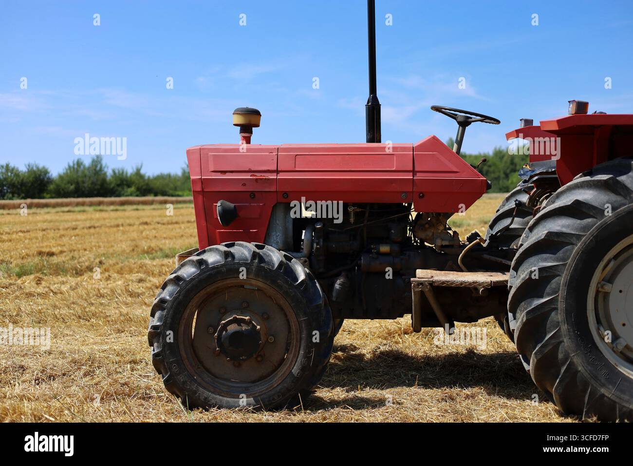 Seitenansicht eines alten, roten Traktors mit sichtbarem Motor, der auf dem gemähten Weizenfeld geparkt ist Stockfoto