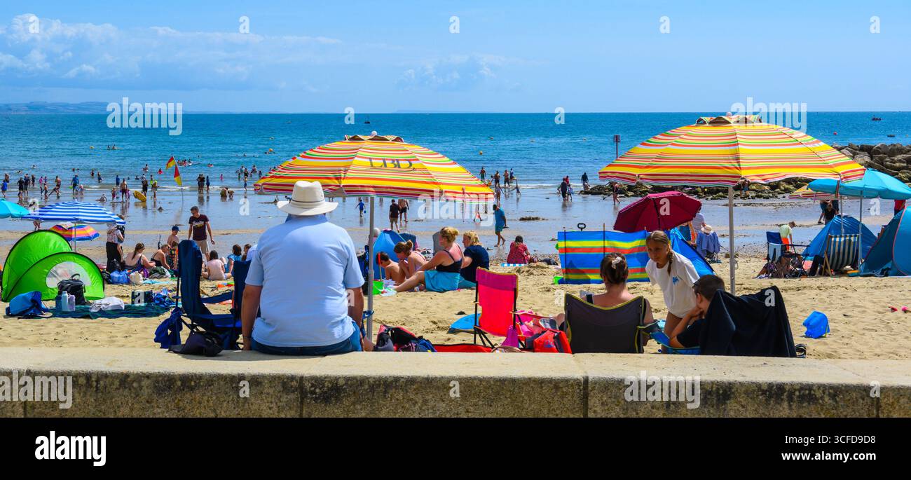 Lyme Regis, Dorset, Großbritannien. August 2025. Wetter in Großbritannien: Die Leute sitzen in Liegestühlen und entspannen unter Sonnenschirmen bei herrlich heißem Sonnenschein, während das Sommerwochenende im August beginnt. Quelle: Celia McMahon/Alamy Live News Stockfoto