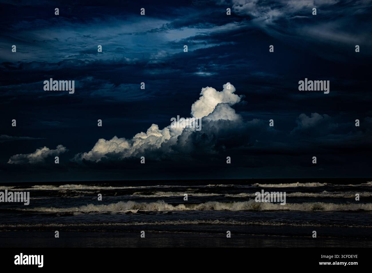 Night Surf II Eine dramatische Meereslandschaft mit abstürzenden Wellen unter einem dunklen, stürmischen Himmel mit aufragenden, beleuchteten Wolken. Stockfoto
