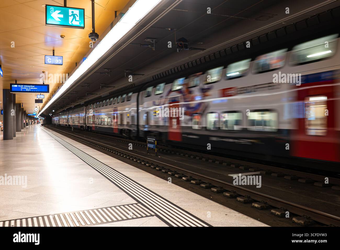 Zürich, Schweiz, 19. August 2025. Verschwommener, fahrender Personenzug, der im unterirdischen Bahnsteig wartet Stockfoto