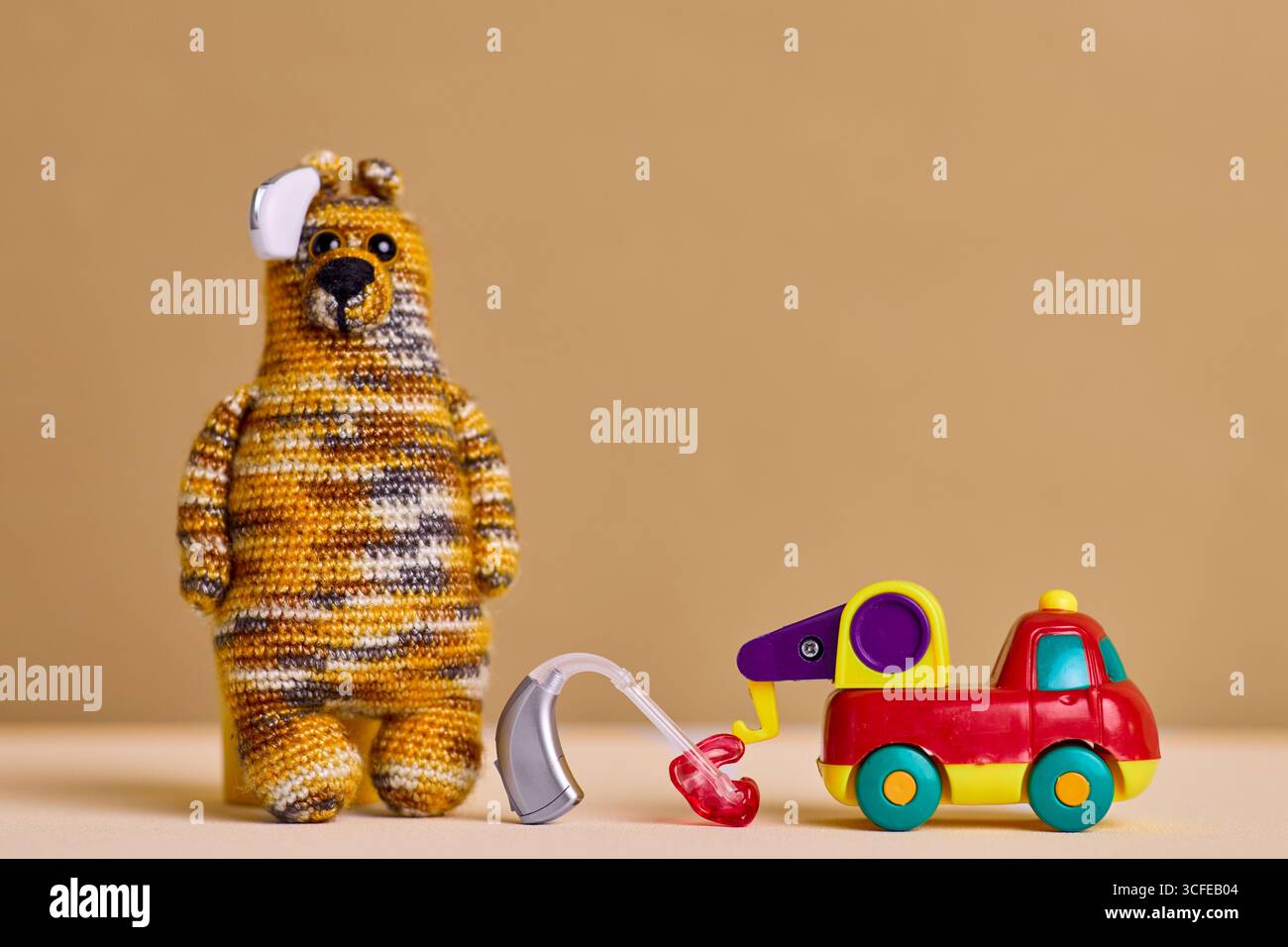Kinderaudiologie. Ein kreatives Hörgerät für Kinder steht neben einem hellen Spielzeugauto und einem Kuschelbären und fördert so die Geräuschwahrnehmung und das Spiel Stockfoto