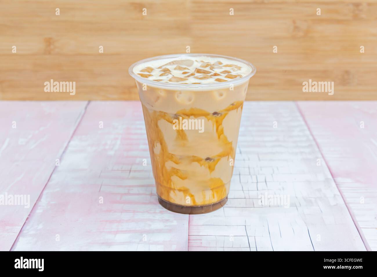 Frische bei jedem Schluck: Nahaufnahme eines Ice Café Latte mit knusprigem Eis und schneereicher Milch, die über den kalten Kaffee gleitet Stockfoto