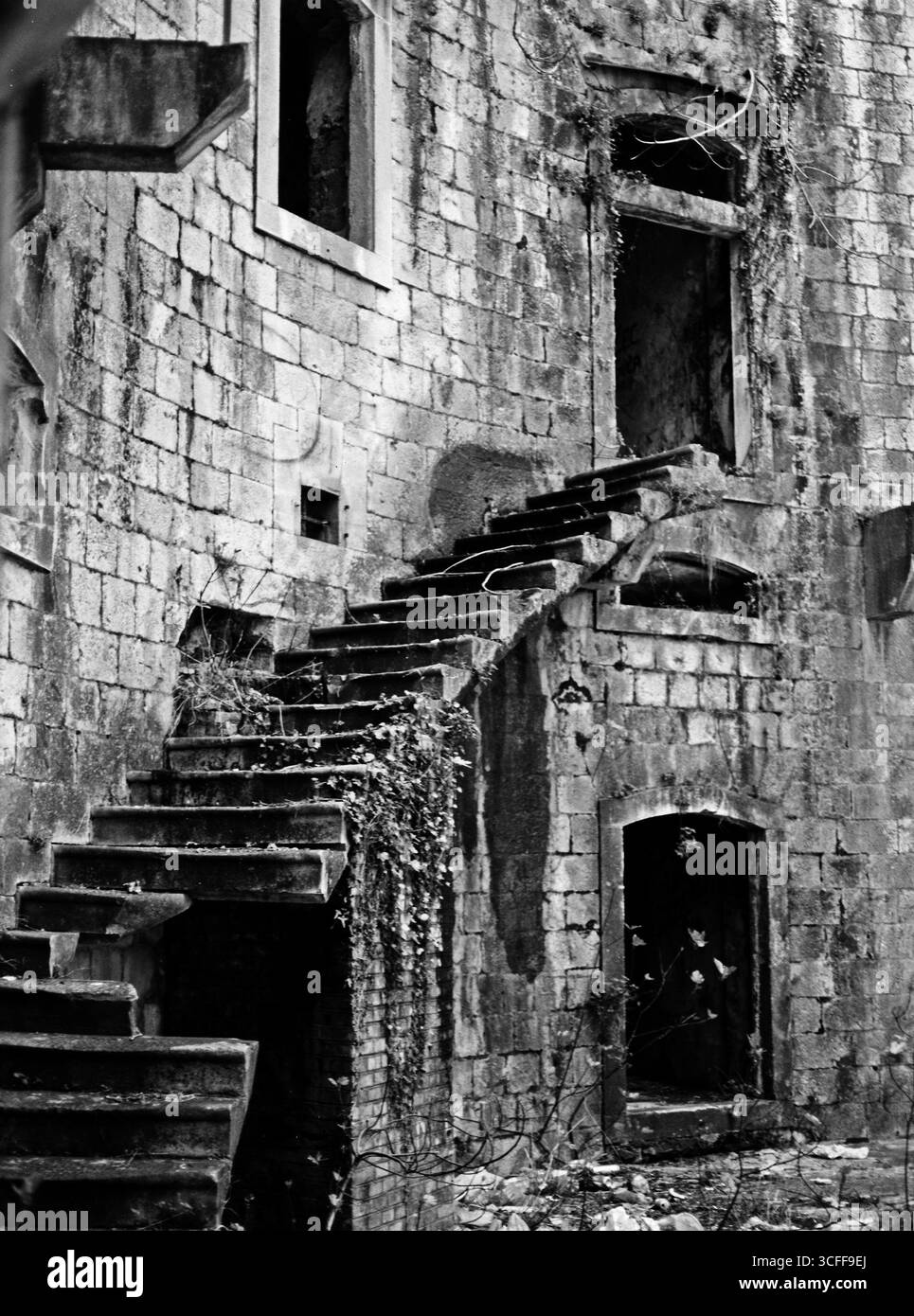Festung. Vertikales Schwarzweiß-Foto im mittleren Format von der Treppe in der verlassenen Mamula-Festung, grelles Licht und Schatten. Stockfoto