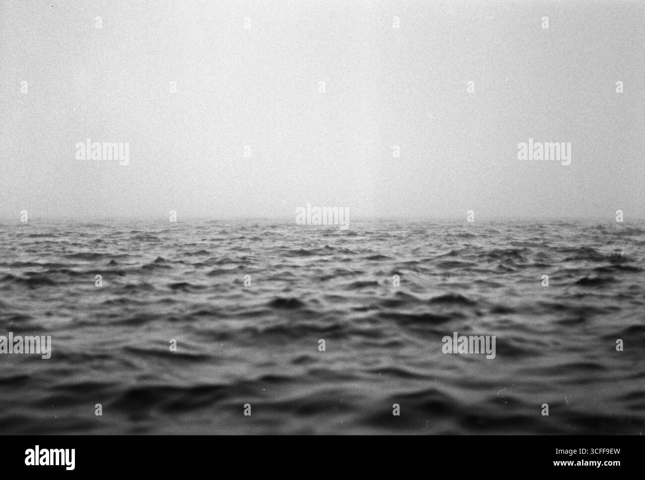 Kein Horizont. Schwarzweiß-Foto im mittleren Format von Wellenmeer unter der Erde und dichtem Nebel, der die obere Hälfte des Rahmens füllt Stockfoto