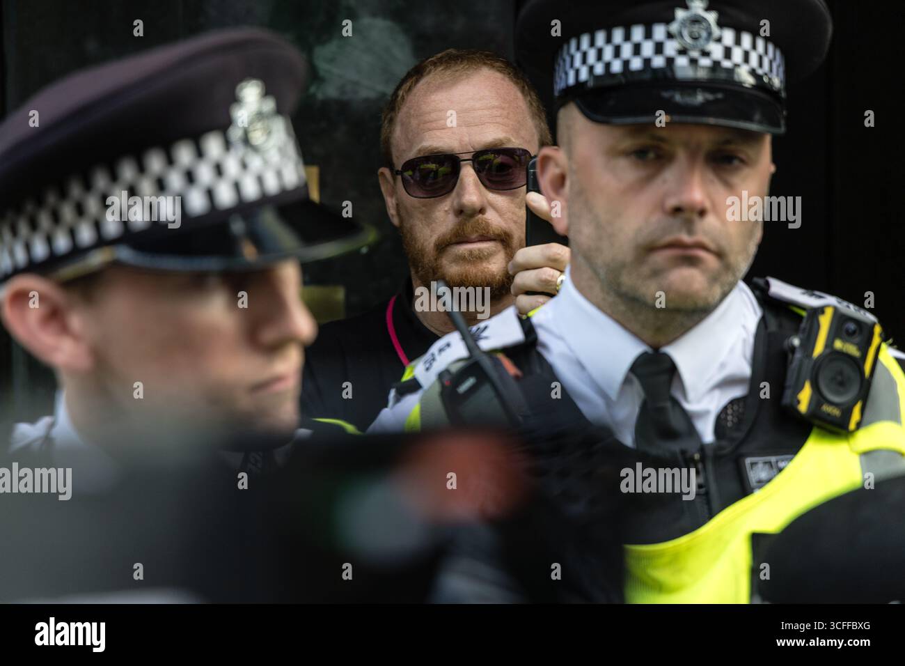 LONDON, UK - 22. August 2025: Polizeibeamte halten einen israelischen Unterstützer in einer Tür fest, während palästinensische Demonstranten während eines Protestes vor der israelischen Botschaft das Gebiet umgeben. Die Aktion, die von der palästinensischen Solidaritätskampagne geleitet wurde, forderte einen Waffenstillstand und internationale Intervention, um den Angriff auf Gaza zu stoppen. Stockfoto