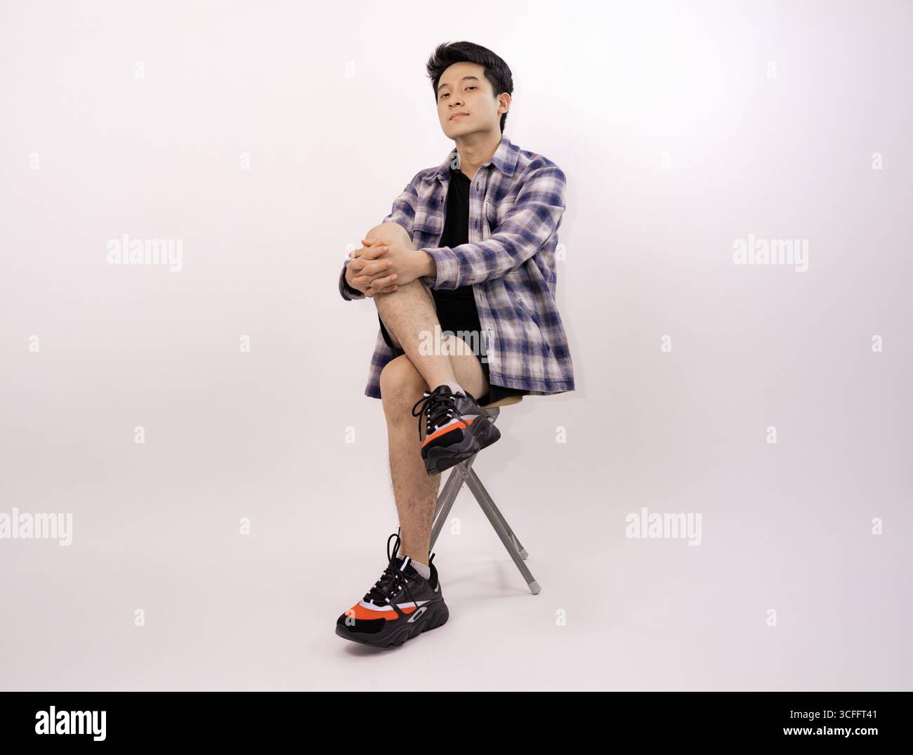 Junger Mann in lässiger Kleidung, der in kontemplativer Pose auf dem Hocker sitzt Stockfoto