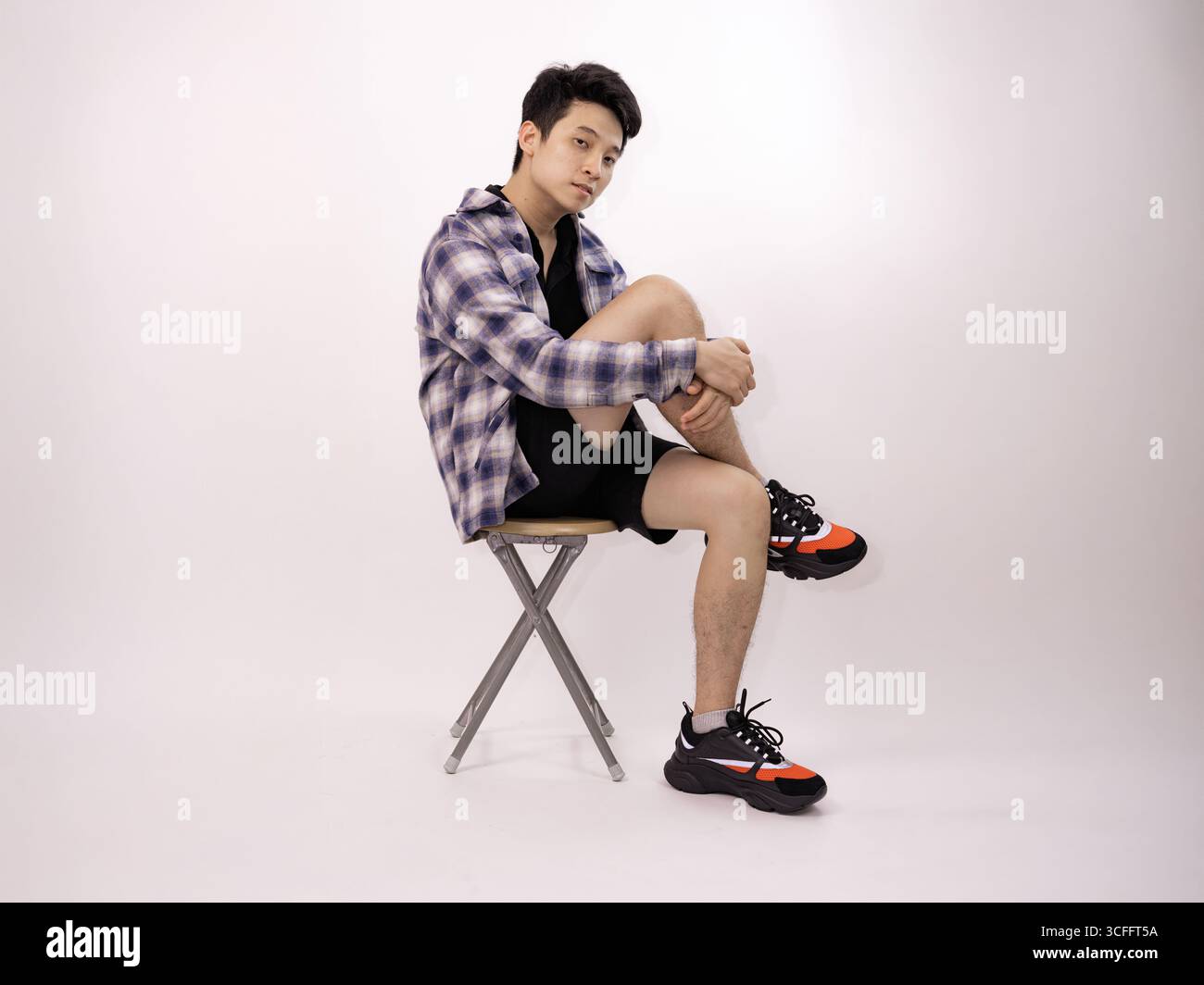 Junger Mann in lässiger Kleidung, der in kontemplativer Pose auf dem Hocker sitzt Stockfoto