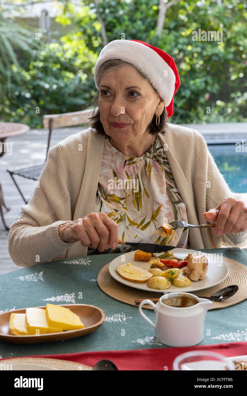 Eine ältere Frau sitzt auf grünem Tischdeck und isst Hühnerkartoffeln auf Teller mit Soßenkanne Stockfoto