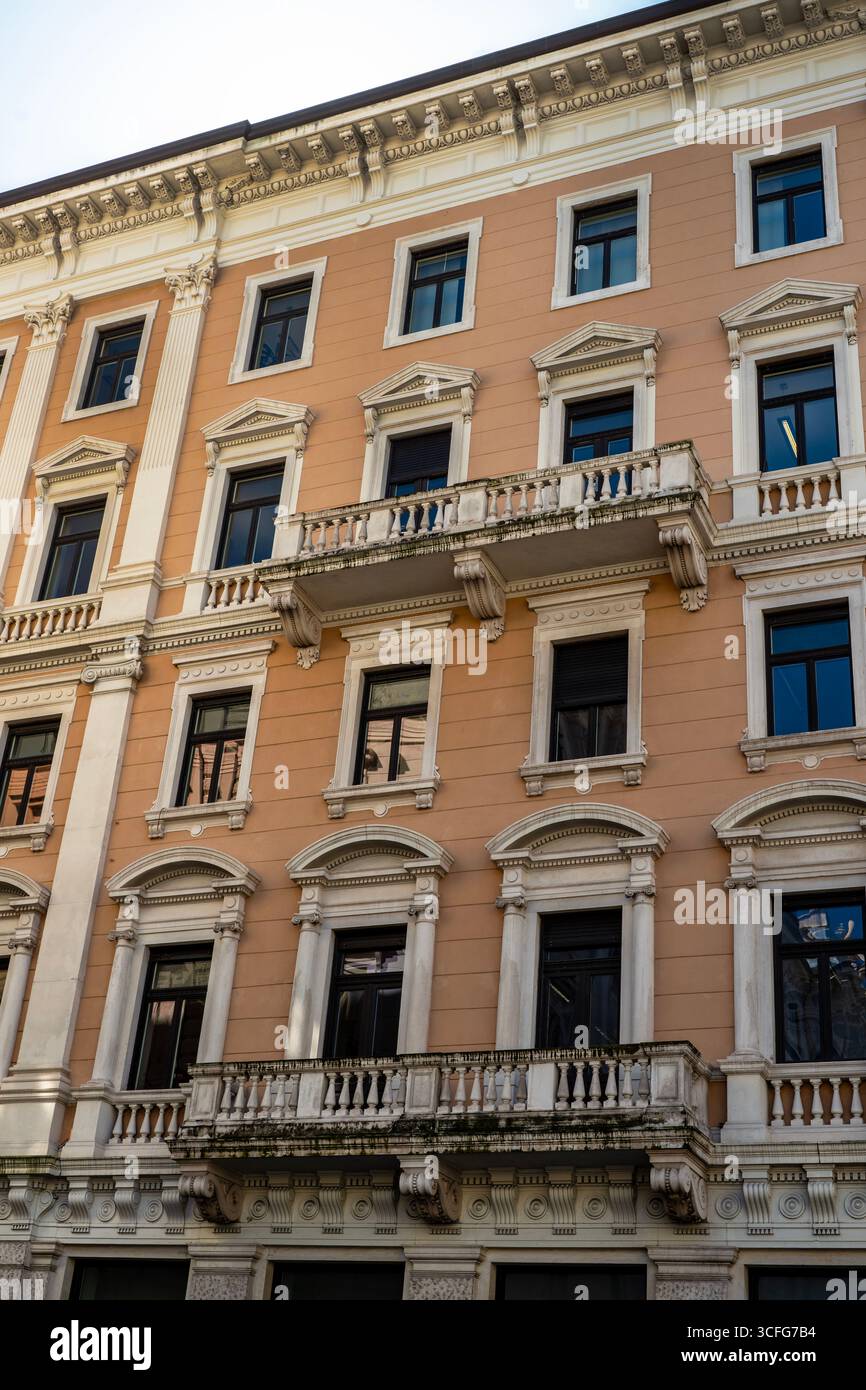 Die neoklassizistische Fassade in Triest, Italien, wird sehr reich mit eklektischen architektonischen Elementen wie runden und gewölbten und trinagulären Giebeln, Stockfoto