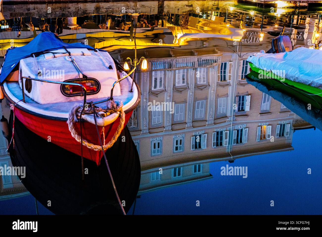 Historischer neoklassizistischer Palast spiegelt den Canal Grande in Triest, Italien, während ein kleines Boot den Weg beleuchtet. Stockfoto