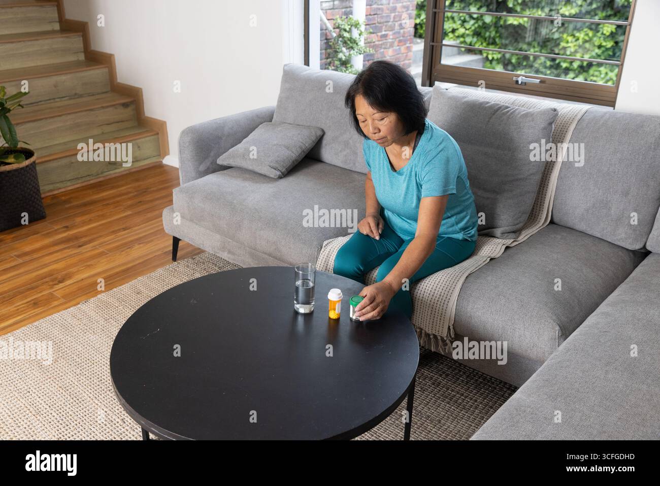 Asiatische Seniorin, die Pillen-Organizer, Pillen-Flaschen auf Couchtisch im Wohnzimmer platziert, Kopierraum Stockfoto