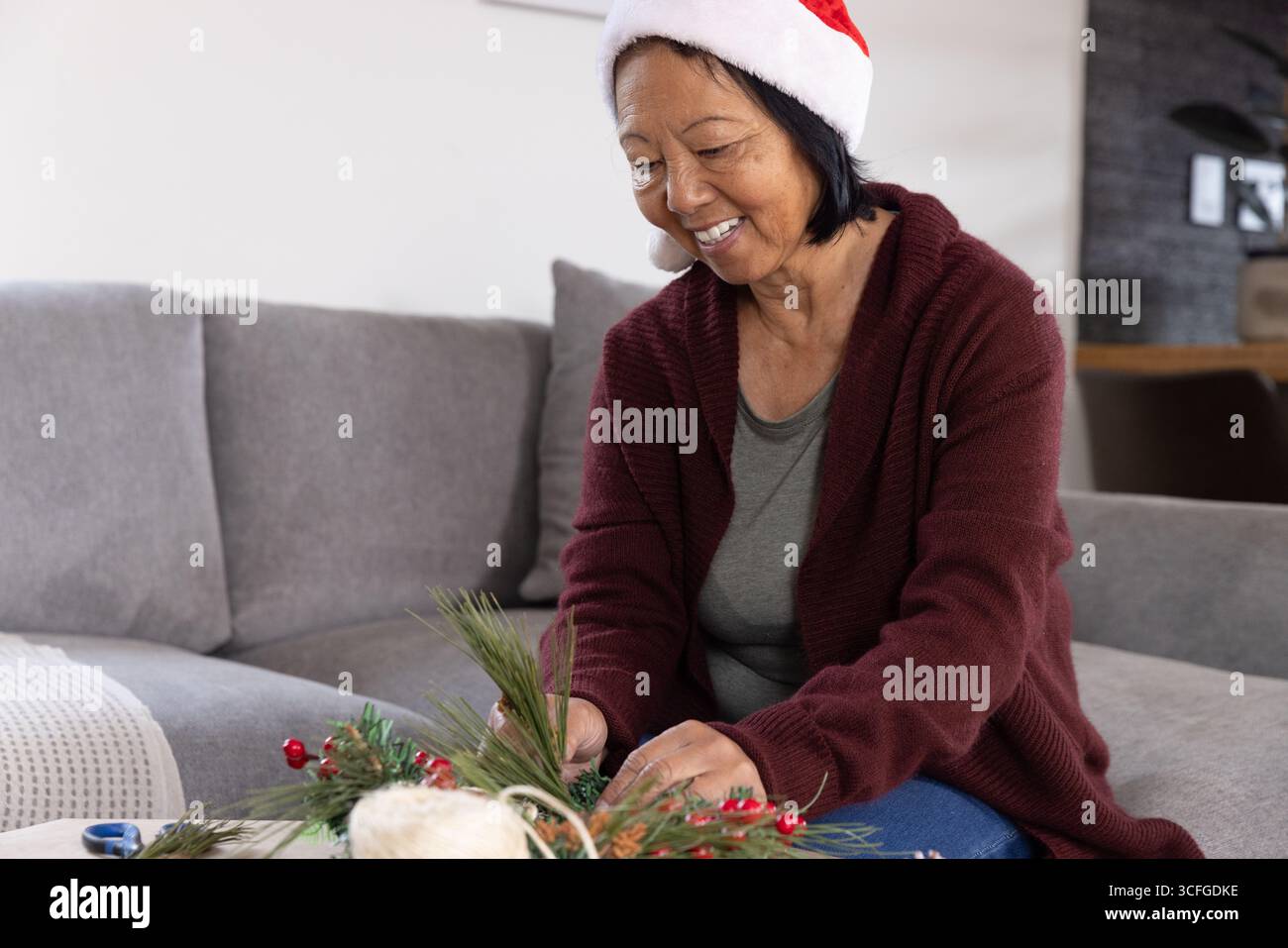 Ältere asiatische Frau mit weihnachtsmütze, die Kiefernzweige und Beeren in den Mittelpunkt stellt Stockfoto