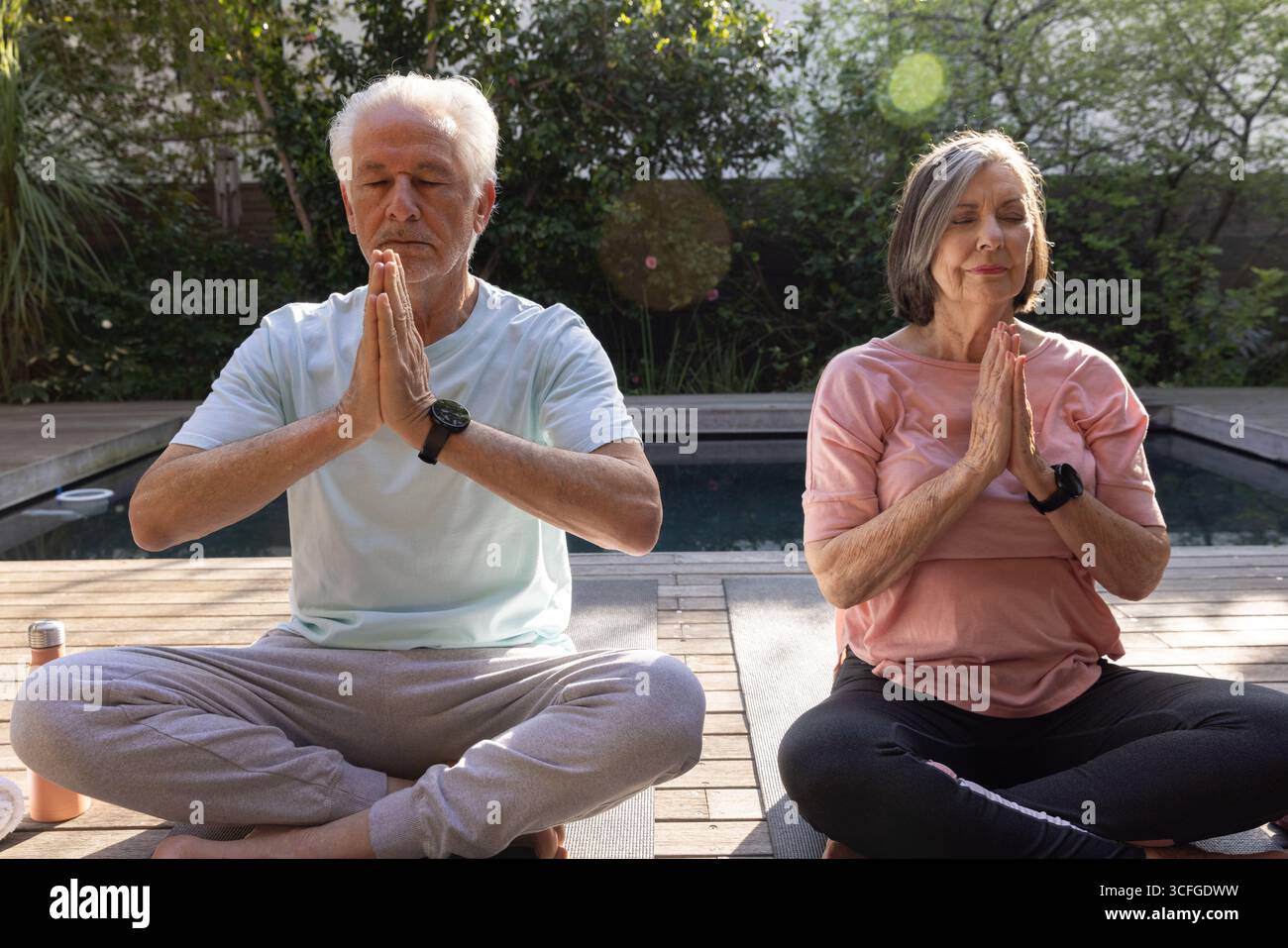 Seniorenpaar üben Meditation auf Deck neben dem Pool mit Yogamatten und Wasserflasche Stockfoto