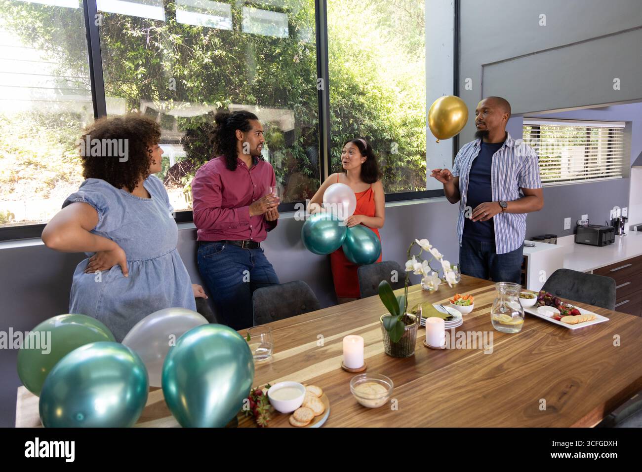 Verschiedene Freunde versammeln sich um einen langen Holztisch im modernen Speisesaal mit Ballons Stockfoto