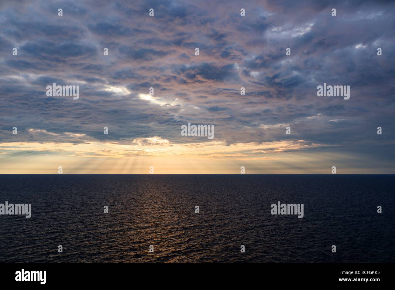 Dramatisch bewölkter Himmel über ruhigem Meer in goldener Stunde mit Sonnenlicht, das durch Wolken bricht Stockfoto