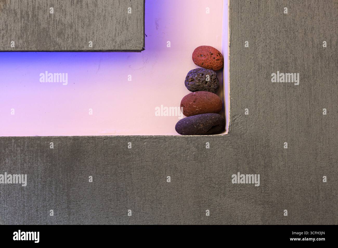 Ästhetische Anordnung von vulkanischen Kieselsteinen in der rechten Ecke einer strukturierten Betonnische. Stockfoto
