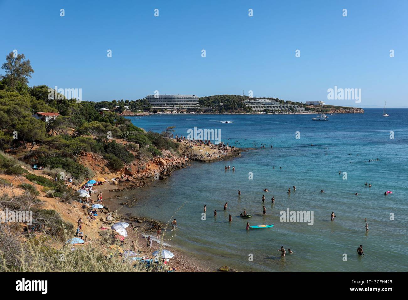 Ein Weitwinkelblick auf den Strand von Paragkes in Vouliagmeni, Athen, Griechenland. Sonnenanbeter und Schwimmer genießen das kristallklare türkisfarbene Wasser umgeben Stockfoto