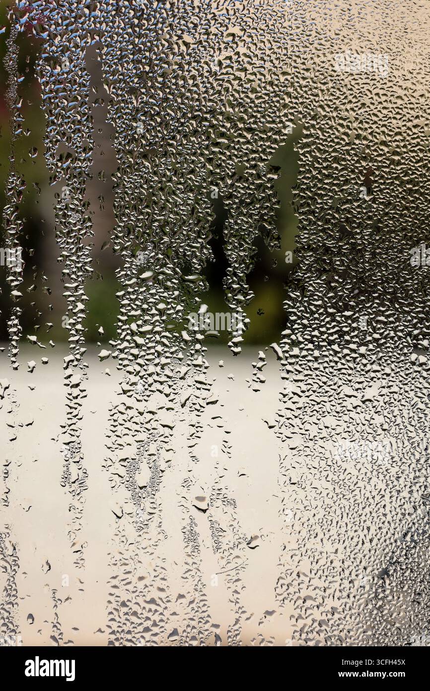Makroansicht von Wassertröpfchen und kondensierter Feuchtigkeit, die abstrakte Streifen auf einer vertikalen Glasoberfläche bilden. Stockfoto