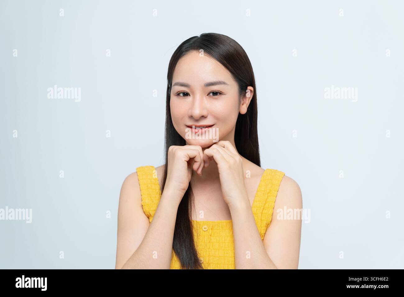 Porträt einer lächelnden Frau, die mit Händen unter dem Kinn posiert und ein gelbes Kleid trägt. Stockfoto