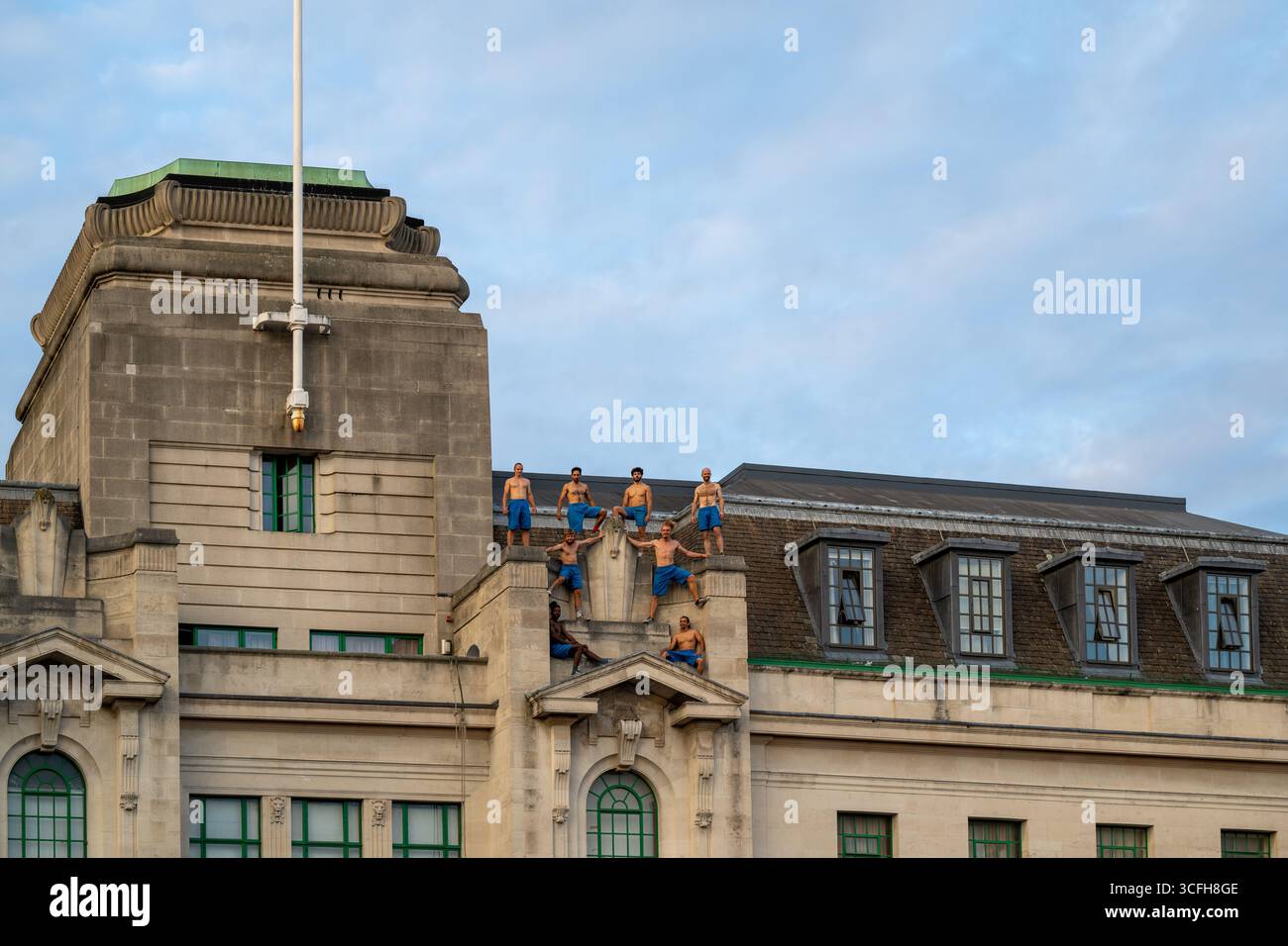 London, Großbritannien, 22. August 2025, begann das Greenwich + Docklands International Festival (GDIF) mit Above and Beyond von Lezards Bleus und The Citizens of the World Choir. Die Menschenmassen überfüllten den Beresford Square in Woolwich, um den acht Darstellern beim Tanz auf den Dächern zuzusehen. Dies ist das 30. Jahr der GDIF, die mit Freilufttheater, Zirkus und Tanz in den Parks feiert. GDIF geht weiter bis zum 8. September. Andrew Lalchan Photography/Alamy Live News Stockfoto