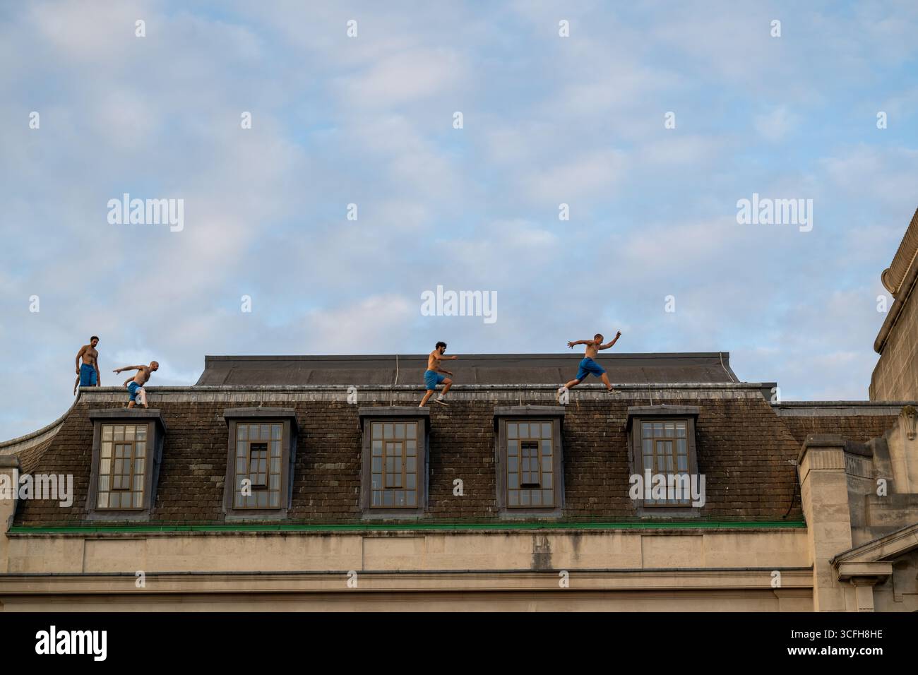 London, Großbritannien, 22. August 2025, begann das Greenwich + Docklands International Festival (GDIF) mit Above and Beyond von Lezards Bleus und The Citizens of the World Choir. Die Menschenmassen überfüllten den Beresford Square in Woolwich, um den acht Darstellern beim Tanz auf den Dächern zuzusehen. Dies ist das 30. Jahr der GDIF, die mit Freilufttheater, Zirkus und Tanz in den Parks feiert. GDIF geht weiter bis zum 8. September. Andrew Lalchan Photography/Alamy Live News Stockfoto