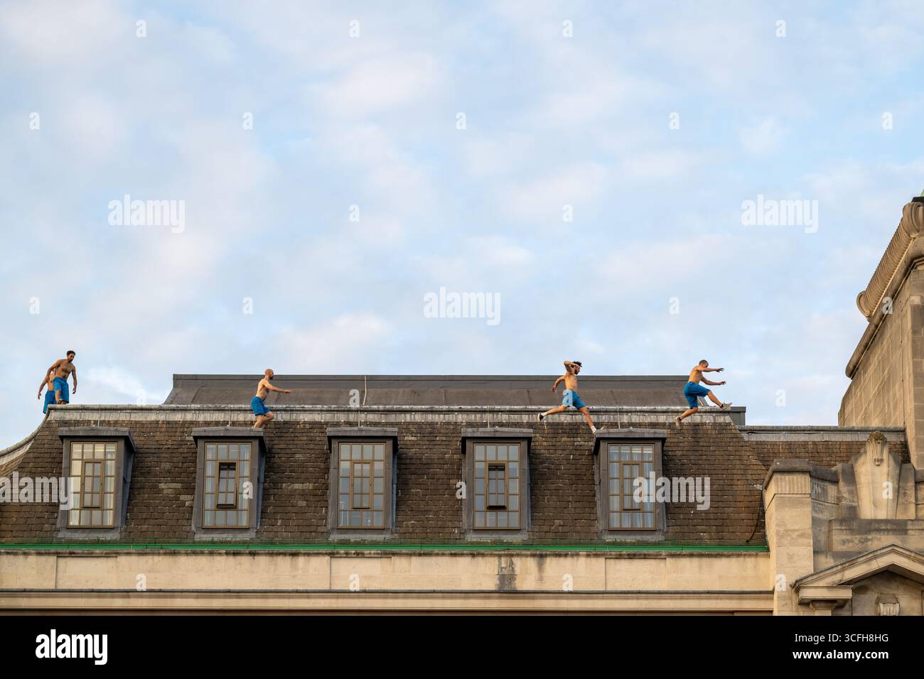 London, Großbritannien, 22. August 2025, begann das Greenwich + Docklands International Festival (GDIF) mit Above and Beyond von Lezards Bleus und The Citizens of the World Choir. Die Menschenmassen überfüllten den Beresford Square in Woolwich, um den acht Darstellern beim Tanz auf den Dächern zuzusehen. Dies ist das 30. Jahr der GDIF, die mit Freilufttheater, Zirkus und Tanz in den Parks feiert. GDIF geht weiter bis zum 8. September. Andrew Lalchan Photography/Alamy Live News Stockfoto