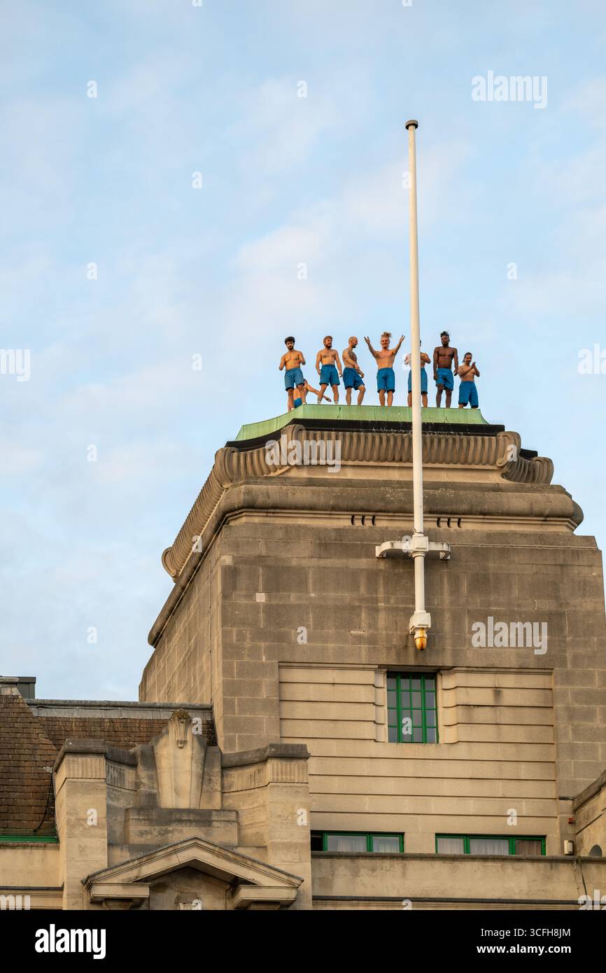 London, Großbritannien, 22. August 2025, begann das Greenwich + Docklands International Festival (GDIF) mit Above and Beyond von Lezards Bleus und The Citizens of the World Choir. Die Menschenmassen überfüllten den Beresford Square in Woolwich, um den acht Darstellern beim Tanz auf den Dächern zuzusehen. Dies ist das 30. Jahr der GDIF, die mit Freilufttheater, Zirkus und Tanz in den Parks feiert. GDIF geht weiter bis zum 8. September. Andrew Lalchan Photography/Alamy Live News Stockfoto