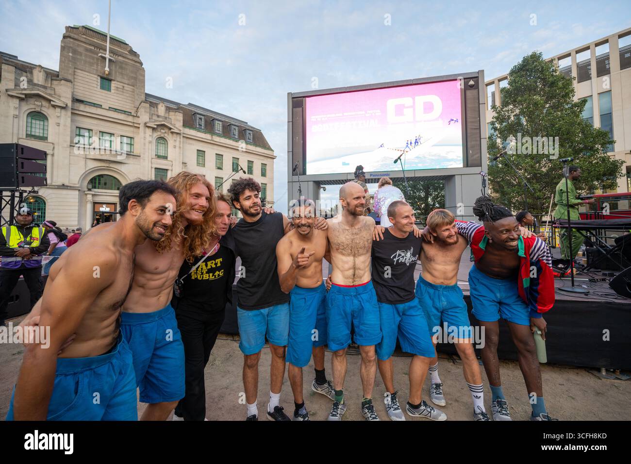London, Großbritannien, 22. August 2025, begann das Greenwich + Docklands International Festival (GDIF) mit Above and Beyond von Lezards Bleus und The Citizens of the World Choir. Die Menschenmassen überfüllten den Beresford Square in Woolwich, um den acht Darstellern beim Tanz auf den Dächern zuzusehen. Dies ist das 30. Jahr der GDIF, die mit Freilufttheater, Zirkus und Tanz in den Parks feiert. GDIF geht weiter bis zum 8. September. Andrew Lalchan Photography/Alamy Live News Stockfoto