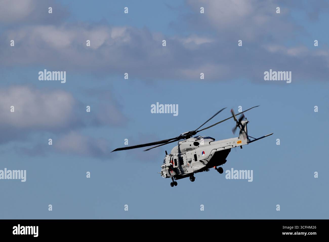 Niederländisches Militär NH90 im Flug über Amsterdam, Niederlande, grauer Seehubschrauber mit offener Seitentür und ausgefahrenem Fahrwerk bei hellem Tageslicht. Stockfoto