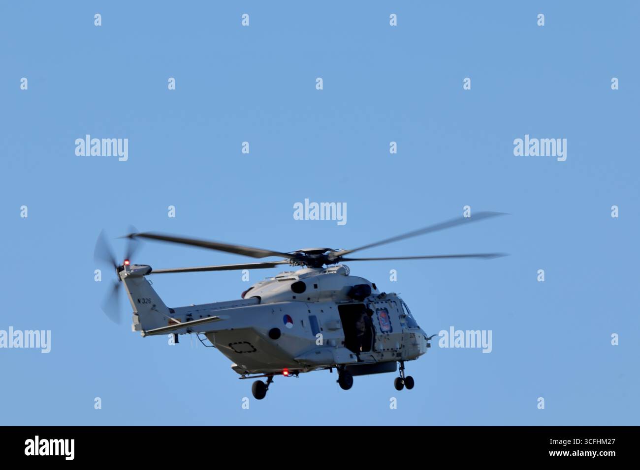 Royal Netherlands Navy NH90 N-326 über Amsterdam, Niederlande, Rückansicht mit Heckrotor, offener Seitentür und Fahrwerk unter klarem Himmel. Stockfoto
