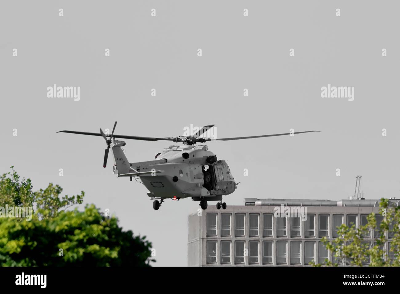 Royal Netherlands Navy NH90 N-326 fliegt tief über Amsterdam, Niederlande, Hubschrauber mit offener Seitentür und Fahrwerk in der Nähe eines Bürogebäudes Stockfoto