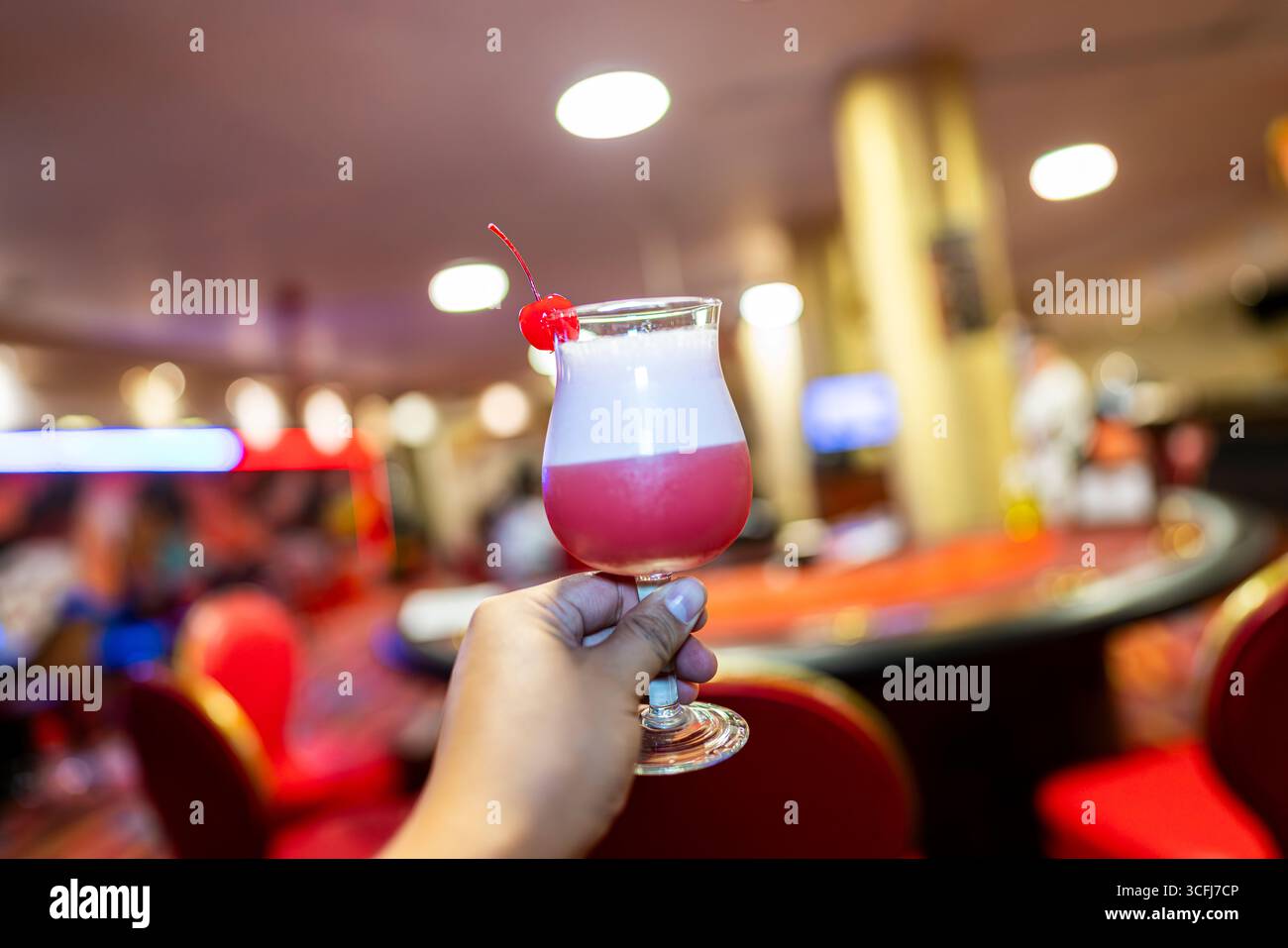 Hand hält rosa Cocktail mit Kirschgarnitur im Casino Stockfoto