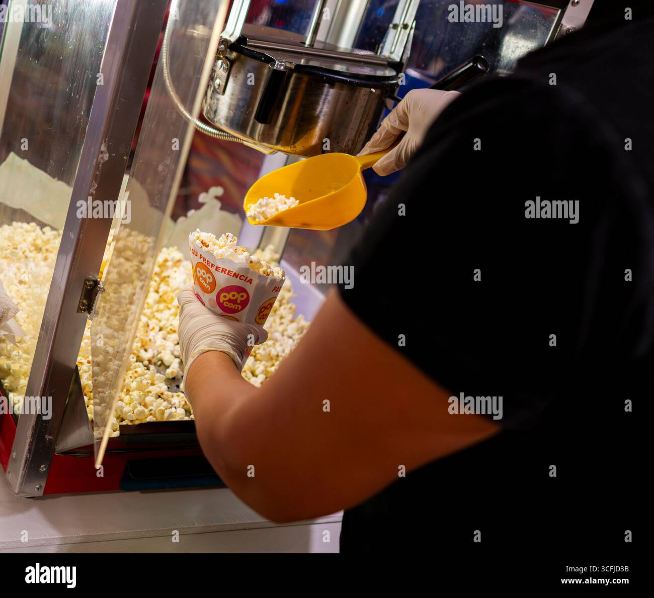 Frisches Popcorn, das aus der Maschine in einem Papierbehälter serviert wird, Nahaufnahme der Zubereitung von Snacks, die Speisen, Kino und Feiern hervorheben. Stockfoto