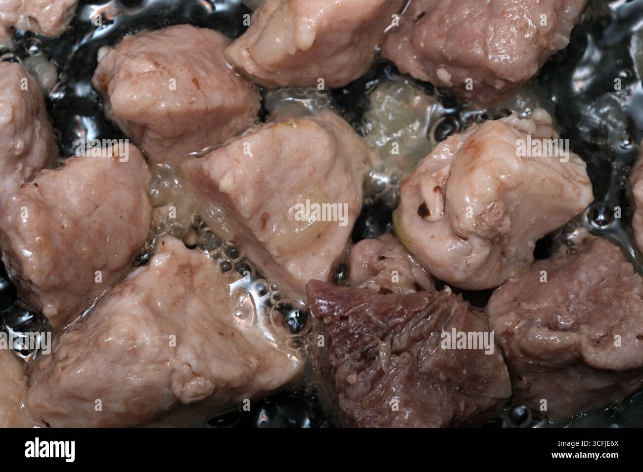 Zarte Fleischstücke werden in sprudelndem Öl gekocht und geben köstliche Aromen in der Küche ab. Stockfoto