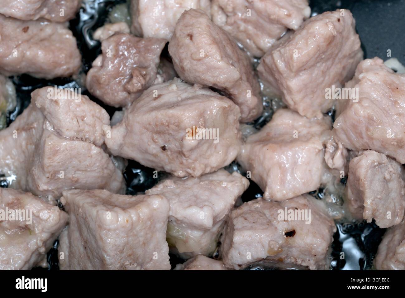 Fleischstücke werden in einer Pfanne gekocht und geben herzhafte Düfte und Säfte frei. Stockfoto