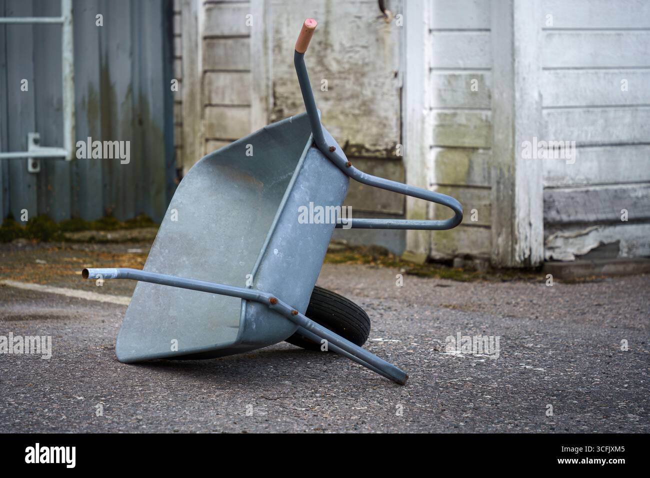 Eine Schubkarre liegt auf ihrer Seite außerhalb eines alten Industriebaus. Stockfoto