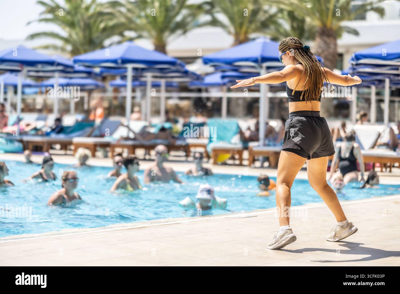 Eine junge weibliche Sportanimatorin macht Wassergymnastik für Menschen im Pool eines Hotelresorts. Stockfoto