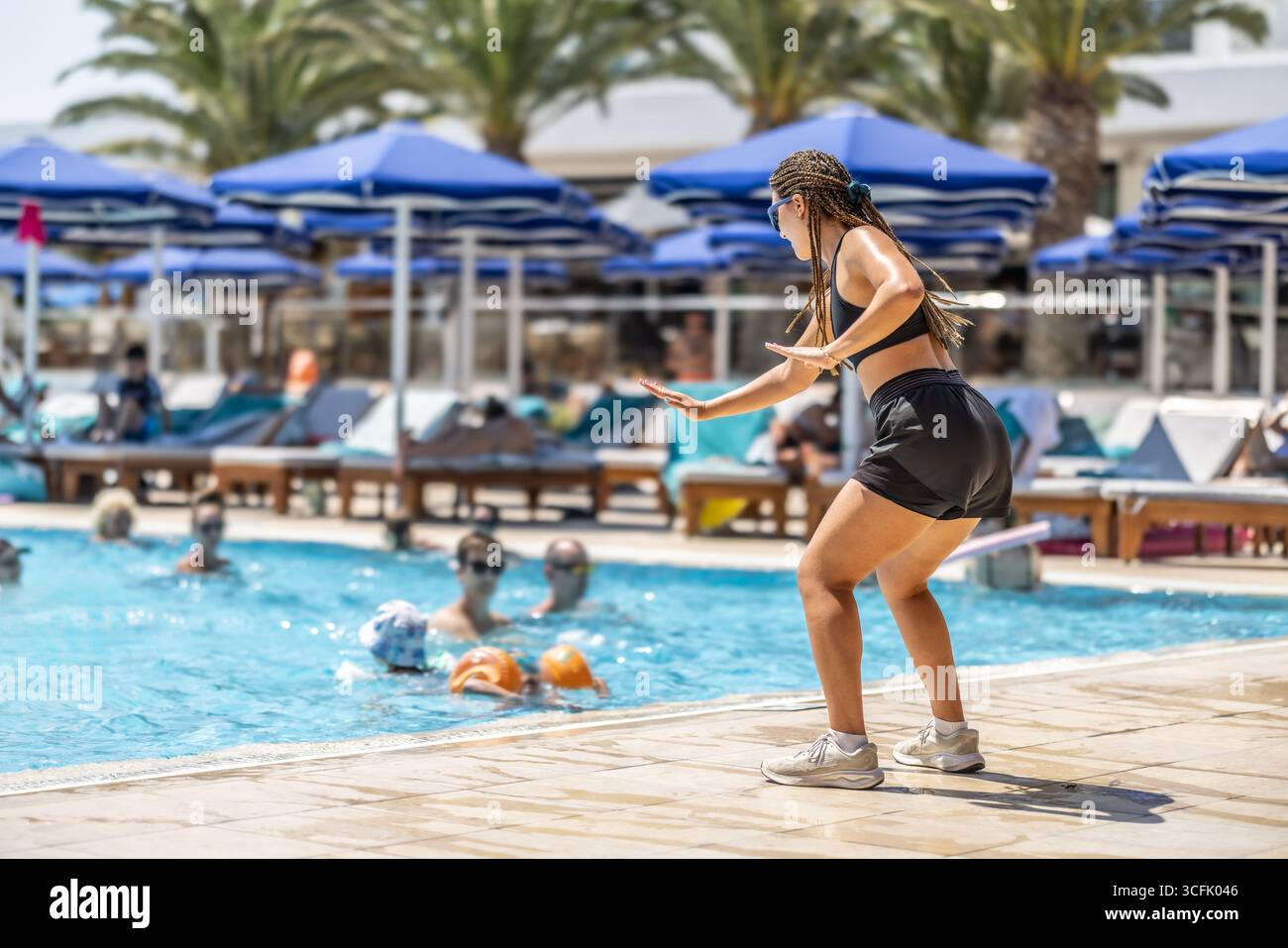 Eine junge weibliche Sportanimatorin macht Wassergymnastik für Menschen im Pool eines Hotelresorts. Stockfoto