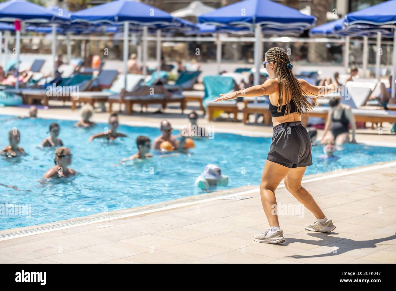 Eine junge weibliche Sportanimatorin macht Wassergymnastik für Menschen im Pool eines Hotelresorts. Stockfoto